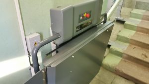 Flīzēta dušas zona ar lietus dušas galvu, rokas dušu, saliekamu baltu dušas sēdekli un hromētu atbalsta stieni pie sienas.