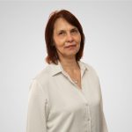 Attēlā sieviete tumšiem matiem un baltā blūzē.