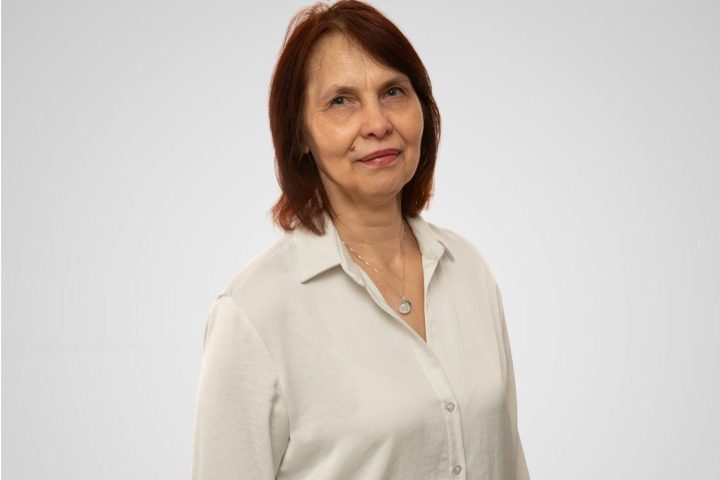 Attēlā sieviete tumšiem matiem un baltā blūzē.