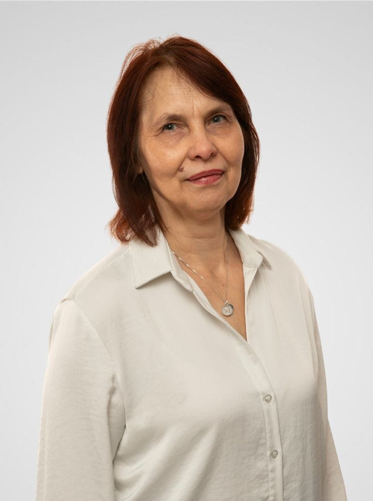 Attēlā sieviete tumšiem matiem un baltā blūzē.