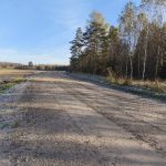 Līkumots zemesceļš ar apsarmojušu zāli malās saulainā rudens dienā. Labajā pusē mežs, kreisajā – lauks ar elektrolīnijām.