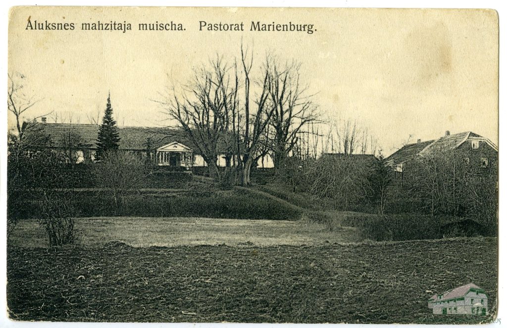 ALUKSNES MAHZITAJA MUISCHA. Pastorat Marienburg. Vēsturiska sēpijas toņa fotogrāfija attēlo lauku ainavu ar vairākām ēkām, tostarp garu māju ar kolonnu portiku, ko ieskauj kaili koki un aramzeme priekšplānā.