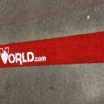 Asfalta segums ar sarkanu līniju, uz kuras baltā krāsā uzkrāsots logotips un teksts "WORLD.com". Kreisajā pusē ir zaļa zāle.