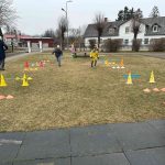 Bērna roka tumši zilā jakā stiepjas pelēkā grozā, kurā ir krāsainas Lieldienu tēmas puzles detaļas. Detaļās redzamas rotātas olas ar ziedu, svītru un punktu rakstiem, kā arī multfilmu dzīvnieki, piemēram, zaķi un vardes. Uz dažām detaļām ir skaitļi, piemēram, "6" un "3".