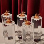 Pieci sešstūraini stikla priekšmeti ar raupju tekstūru un zelta bites figūriņām virspusē. To apakšējā daļa ir tumša, un tie atrodas uz baltas virsmas pret tumši sarkanu samta aizkaru.