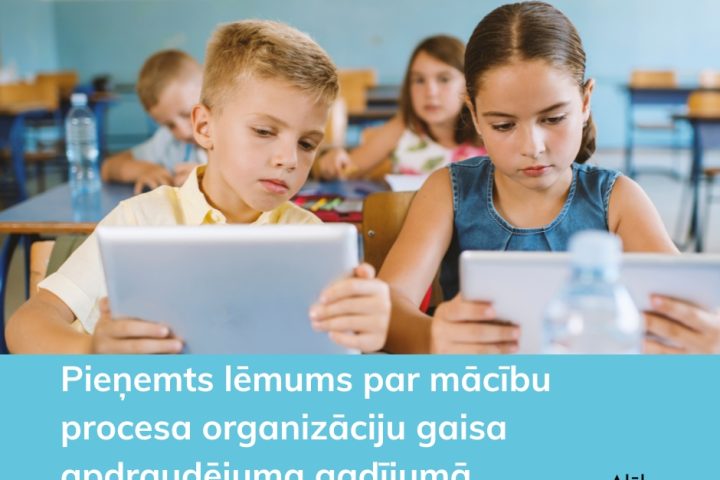 Divi bērni sēž klasē un koncentrēti skatās savos planšetdatoros. Attēlā redzamais teksts: Pieņemts lēmums par mācību procesa organizāciju gaisa apdraudējuma gadījumā. Alūksne Oinkaua.