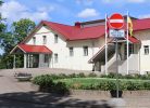 Gaiši dzeltena ēka ar sarkanu jumtu un vairākām ieejām. Priekšplānā bruģēts celiņš un apstādījumi. Pie ēkas redzama zīme "Iebraukt aizliegts" ar papildtekstu "Izņemot ar Alūksnes kultūras centra atļauju" un mastos plīvo Latvijas un Ukrainas karogi.