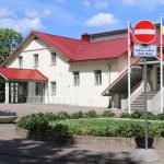 Gaiši dzeltena ēka ar sarkanu jumtu un vairākām ieejām. Priekšplānā bruģēts celiņš un apstādījumi. Pie ēkas redzama zīme "Iebraukt aizliegts" ar papildtekstu "Izņemot ar Alūksnes kultūras centra atļauju" un mastos plīvo Latvijas un Ukrainas karogi.