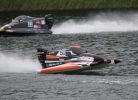 Divas ātrgaitas laivas sacīkstēs uz ūdens. Priekšplānā melna, oranža un balta laiva ar numuru "51" un uzrakstiem "MERCURY", "F1POWERBOAT", "MEMELES" un "22448254", veidojot lielas šļakatas. Aizmugurē pelēka laiva ar numuru "22" un "MERCURY" uz dzinēja.
