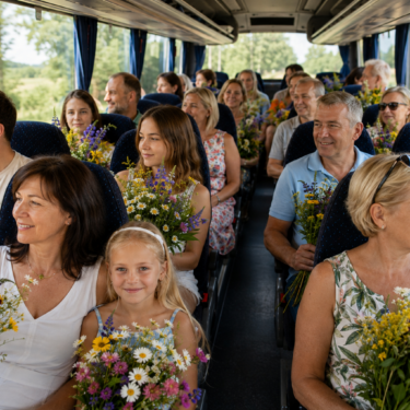 Autobusā sēž dažādu paaudžu cilvēku grupa, kuri smaida un tur rokās krāsainus pļavas ziedu pušķus. Aiz loga redzama zaļa ainava.