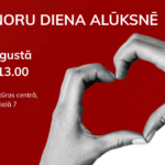 Plakāts ar sarkanu fonu, uz kura divas rokas veido sirds formu. Teksts: "DONORU DIENA ALŪKSNĒ", "18. augustā 9.00-13.00", "Alūksnes Kultūras centrā, Brūža ielā 7". Apakšējā labajā stūrī Valsts asinsdonoru centra logo.