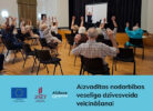 Zālē vecāka gadagājuma cilvēki sēž uz krēsliem un veic vingrojumus ar paceltām rokām, sekojot instruktoram priekšā. Attēlā redzams teksts: "Aizvadītas nodarbības veselīga dzīvesveida veicināšanai", un logotipi "Līdzfinansē Eiropas Savienība", "2027 Nacionālais attīstības plāns", "Alūksne".