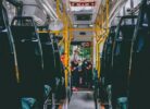 Autobusa salons ar rindām tumšu sēdvietu un dzelteniem rokturiem. Autobusa priekšgalā sieviete gaišā cepurē stāv, mijiedarbojoties ar iekārtu pie autovadītāja sēdvietas. Virs viņas redzams numurs "2166".